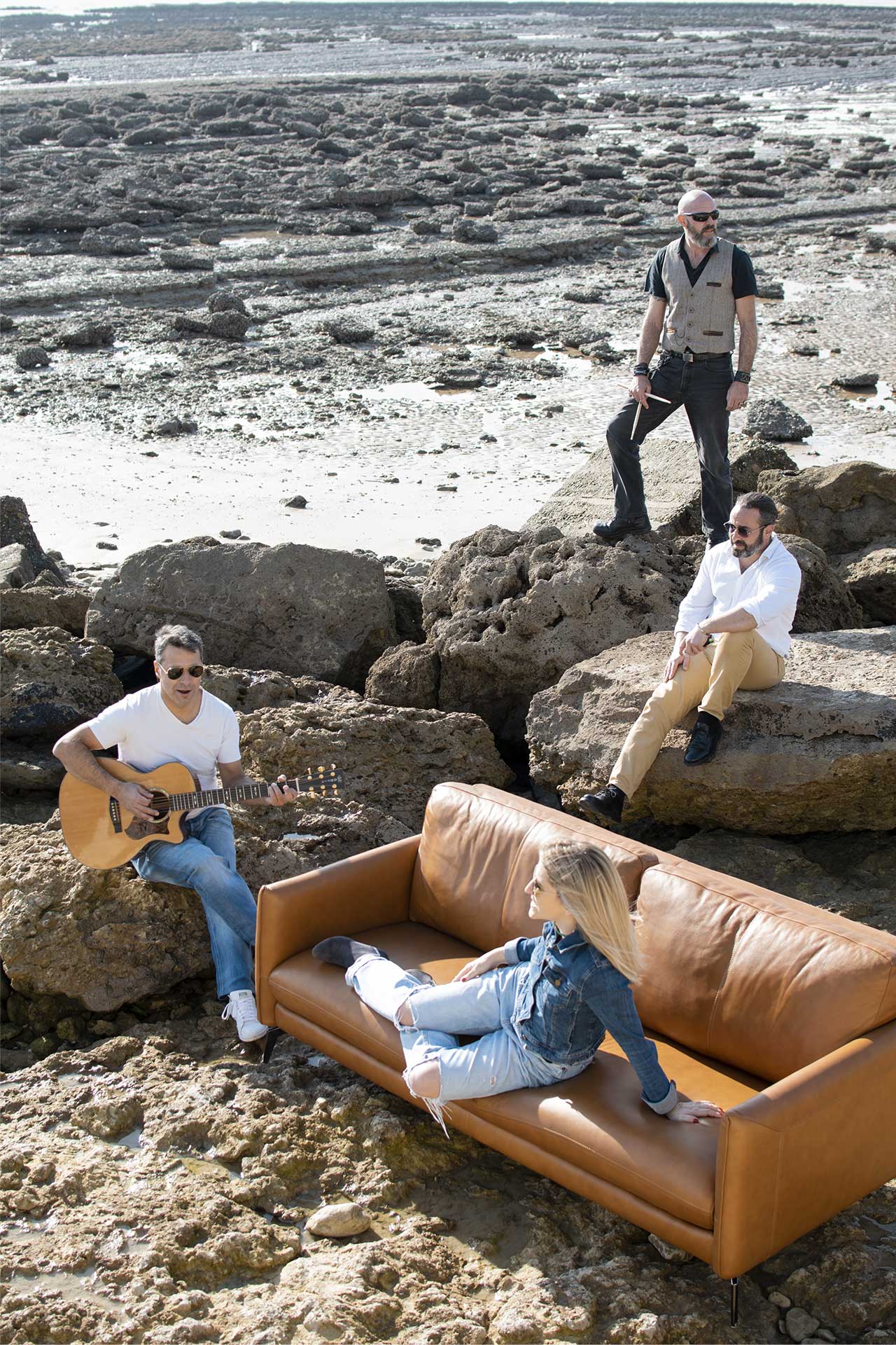 Groupe de musique ROCK'ELLE posant sur le rivage rocheux d'Angoulins avec la chanteuse assise sur un canapé et des musiciens debout et assis avec leurs instruments.