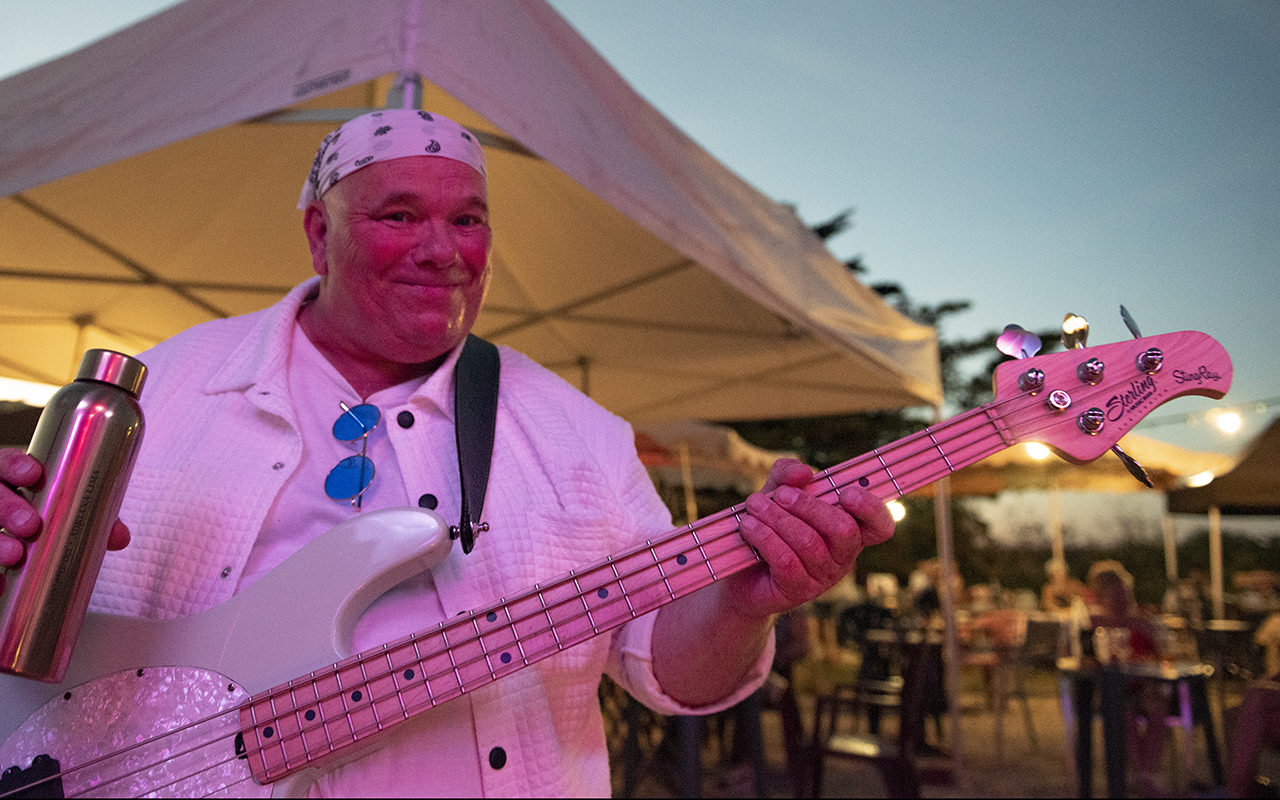 Guitariste de ROCK'ELLE souriant en jouant de la guitare acoustique sur un fond de rochers côtiers à La Rochelle